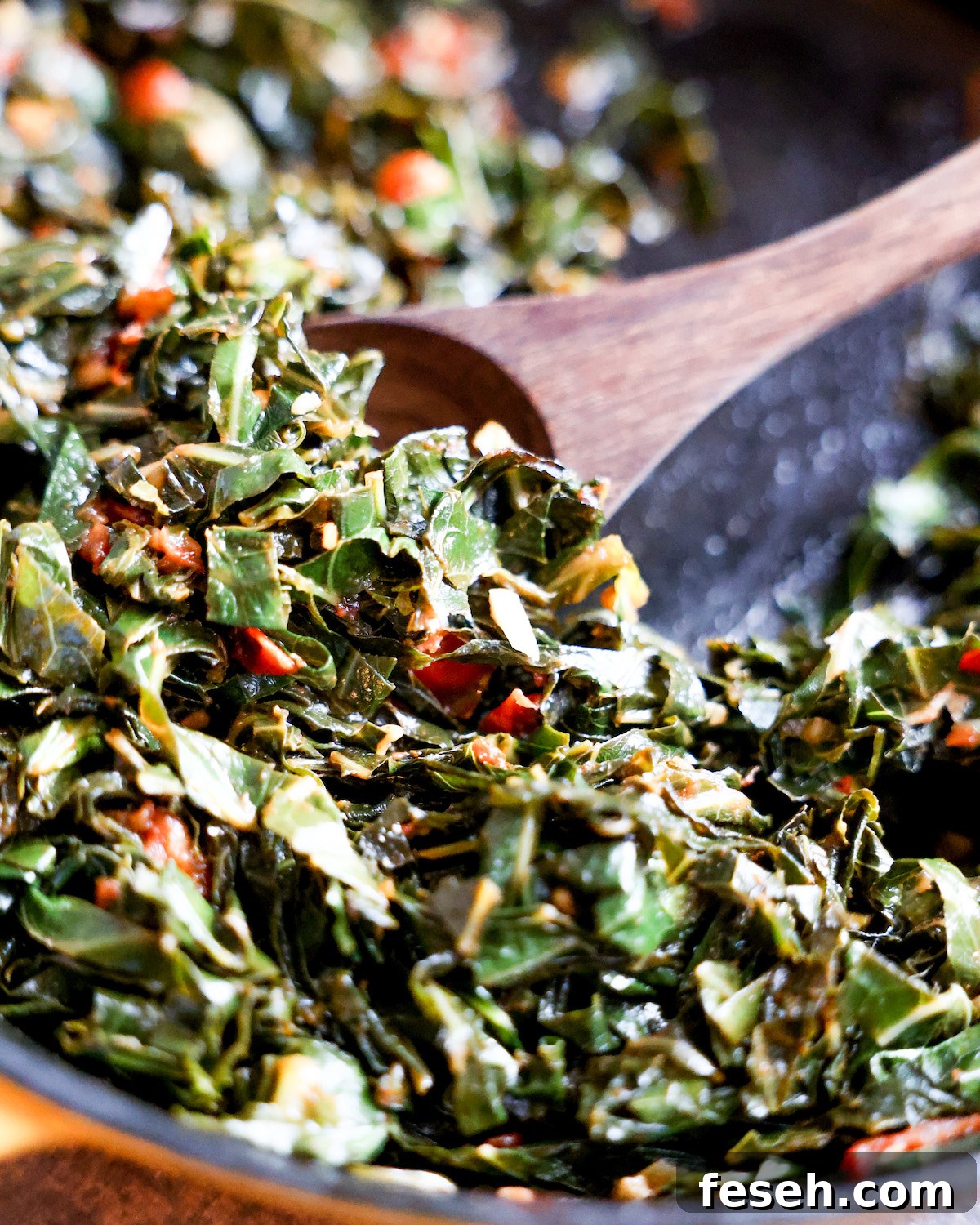 Wooden spoon scooping collard greens in a skillet.