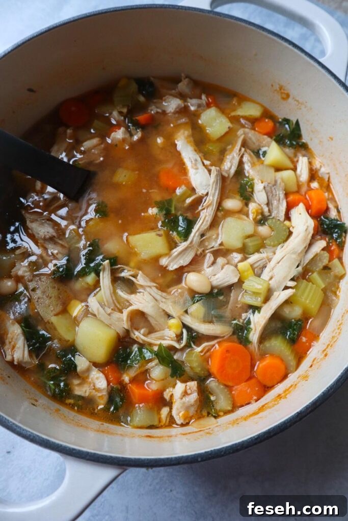 dutch oven with soup with potatoes, chicken, carrots, kale, celery, and garlic