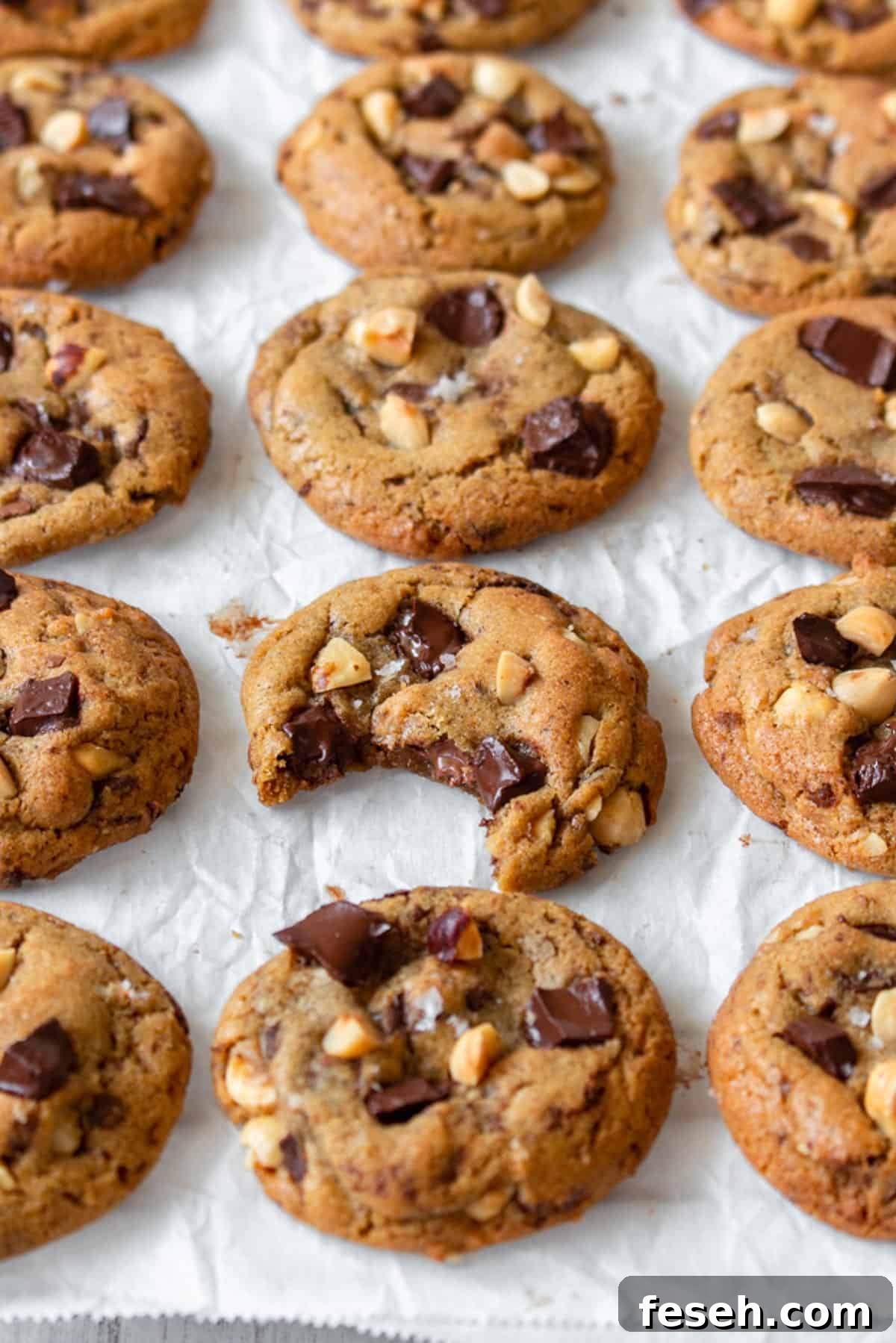 Brown butter chocolate chip cookies laid out in rows, with one having been bitten.