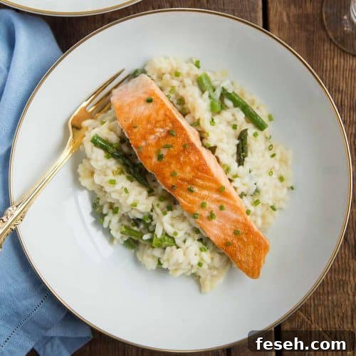 piece of seared salmon on top of asparagus risotto in a white shallow bowl with a gold fork.
