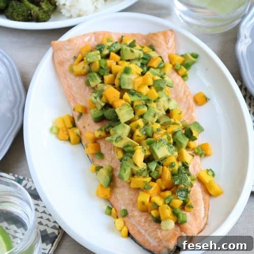 side of salmon on a white platter, topped with a mango and avocado salsa.