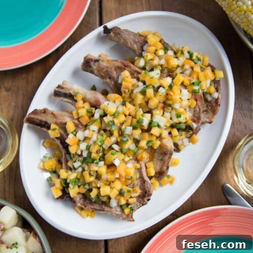 grilled pork chops topped with peach salsa on a white platter.