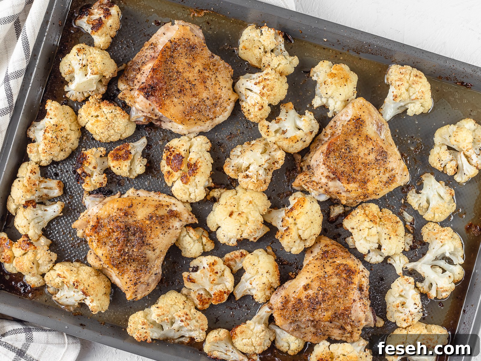 A baking sheet with baked Cajun Chicken Thighs and roasted cauliflower.