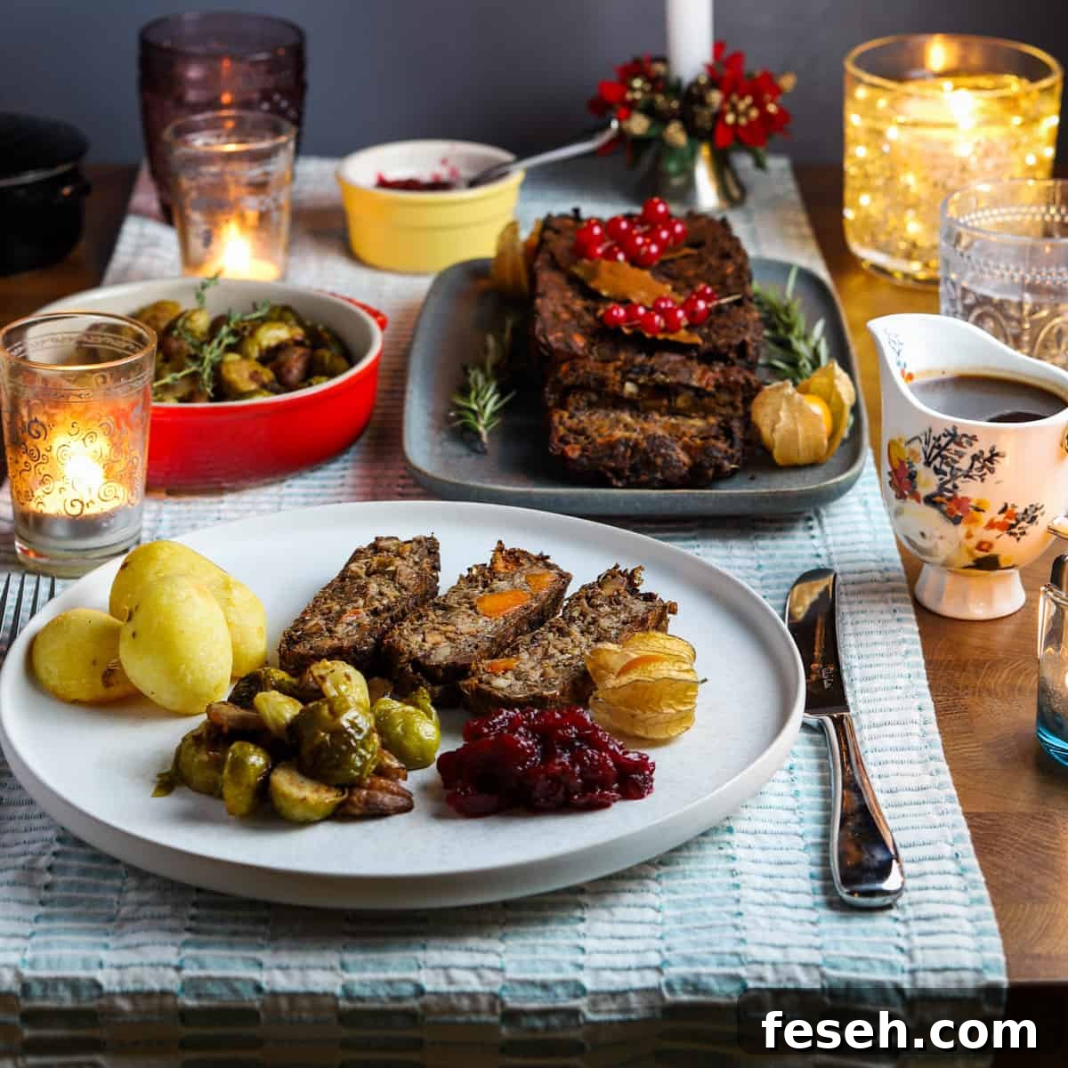 Photo of a tablescape with this vegan nut roast as the centrepiece, a bowl of sprouts, a pretty jug of gravy, a full plate of food in the foreground, and candles dotted around.