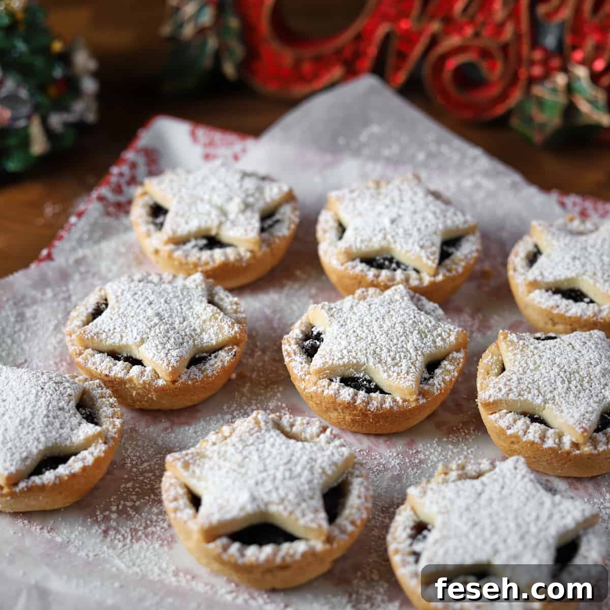 Square photo of 9 star-topped, icing sugar dusted vg gf mince pies with christmas ornaments in the background.