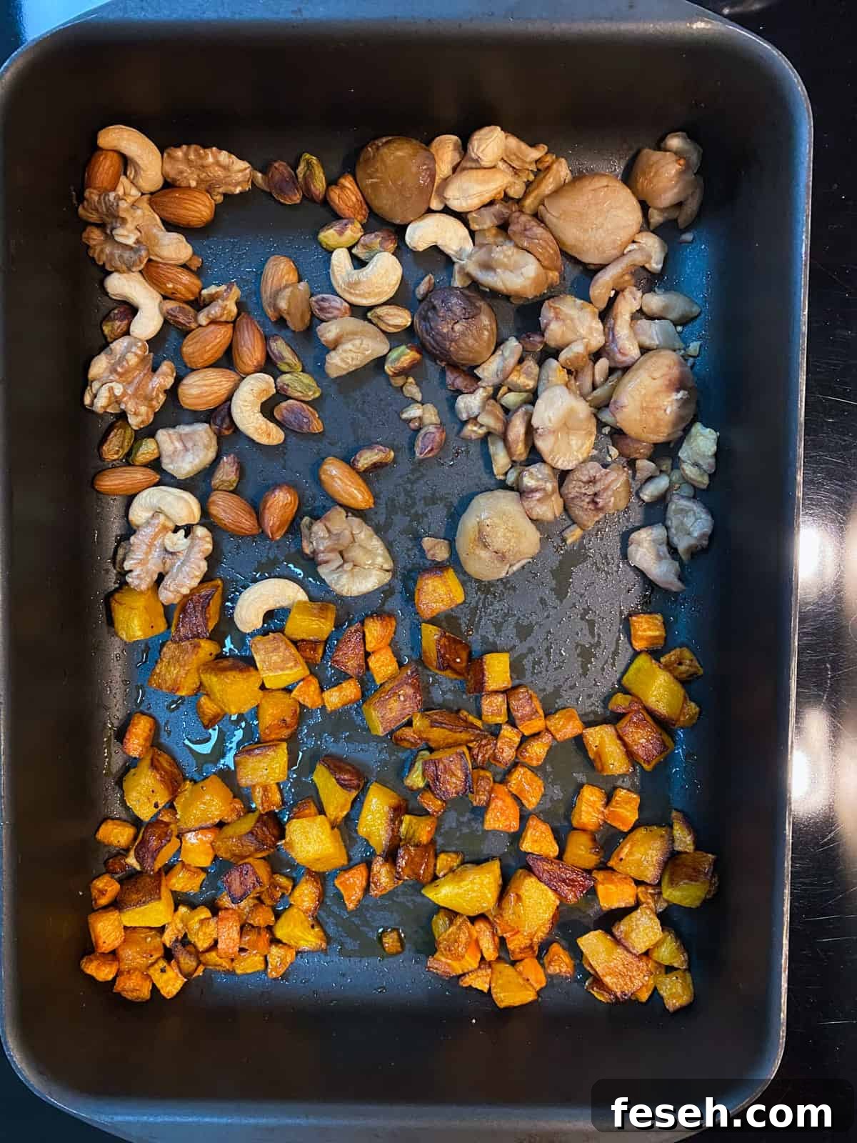 Photo of carrots and butternut squash in a roasting tin and nuts and chestnuts at the other end.