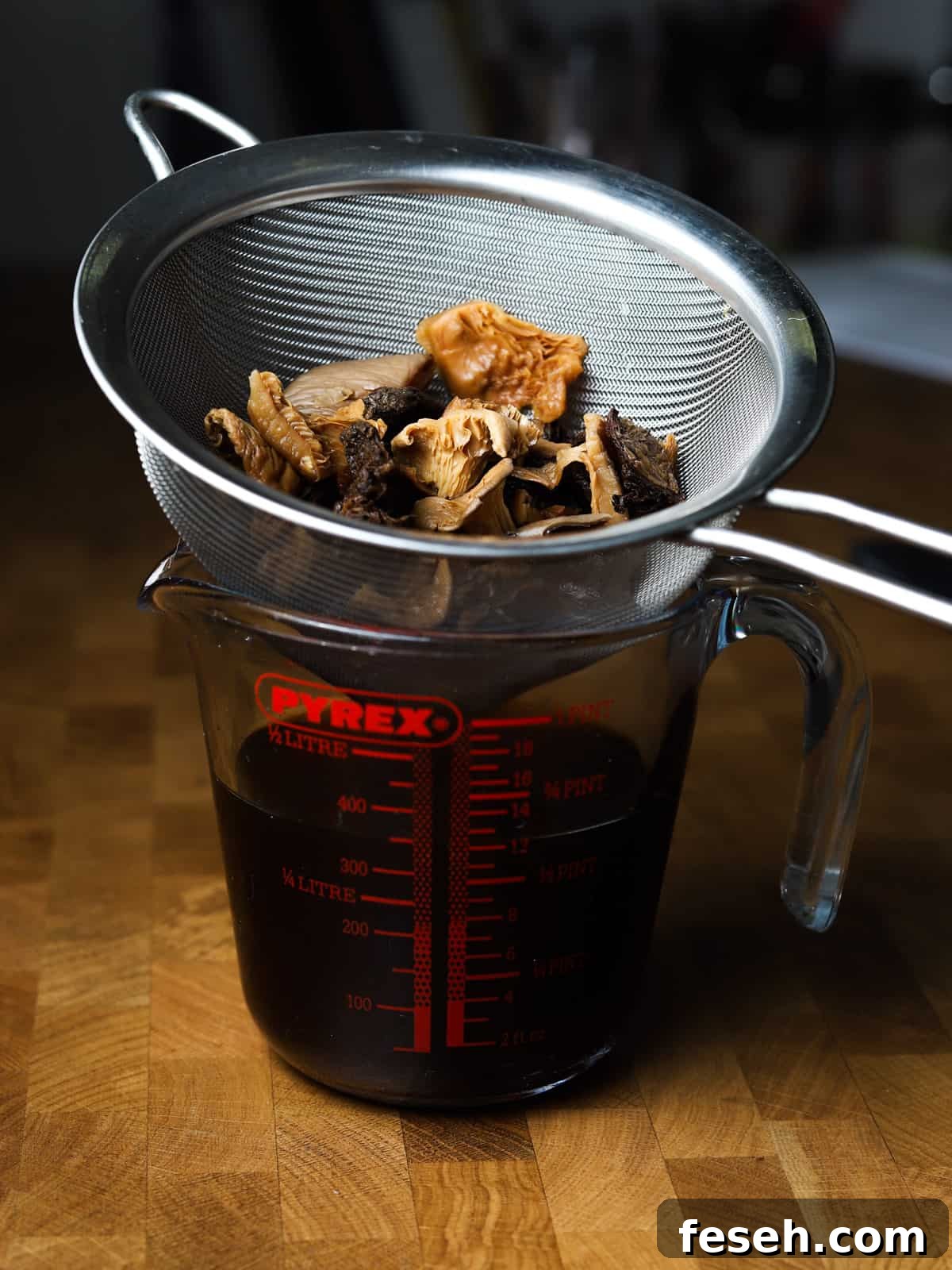 Photo of soaked, dried mushrooms in a sieve with the soaking liquor in a jug underneath.