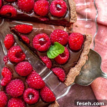 A serving utensil removes a slice of chocolate raspberry tart from a platter.