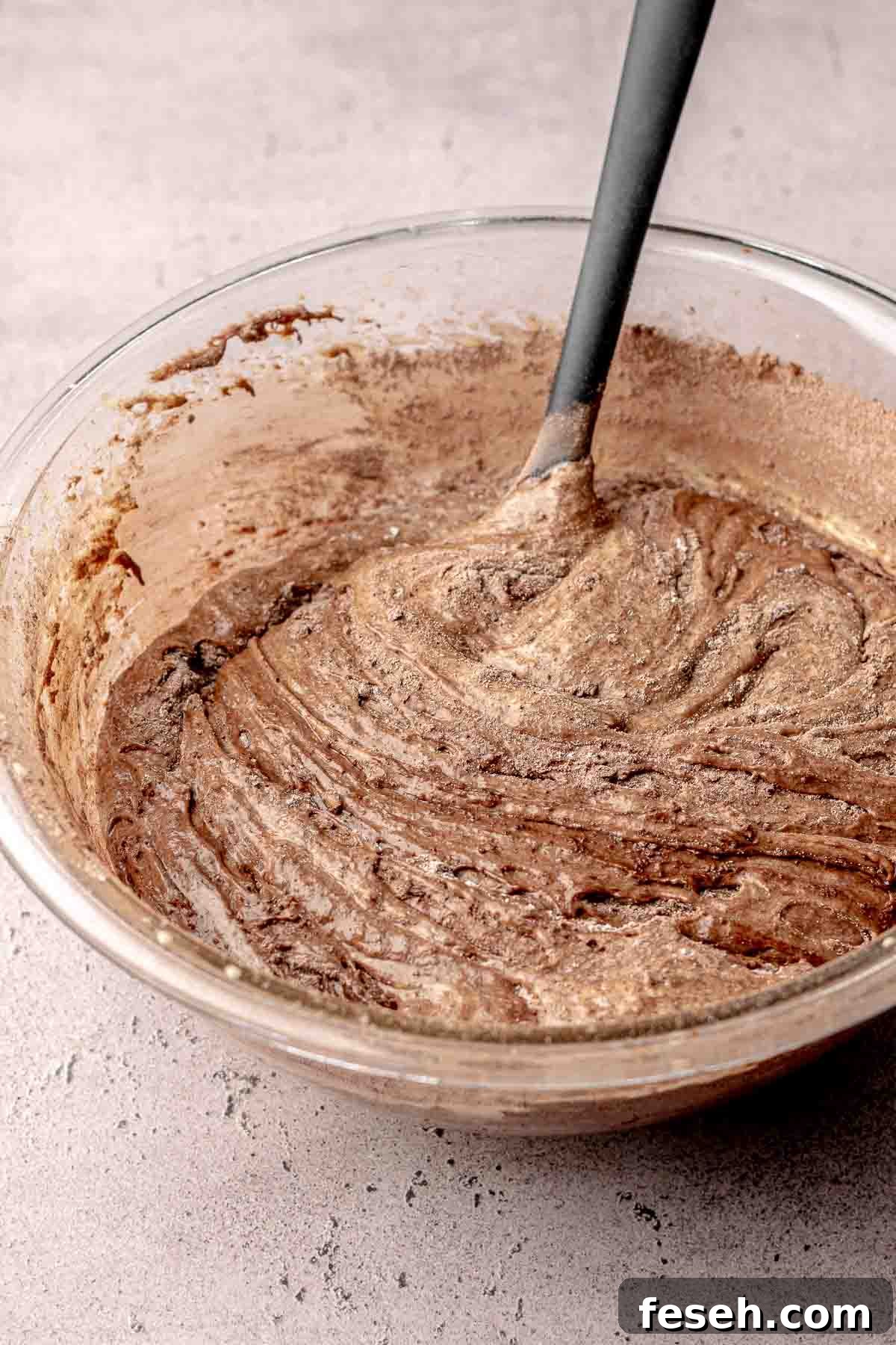 A rubber spatula folds dry ingredients into brownie batter.