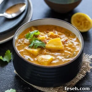 potato curry served in a black bowl, garnished with cilantro with a bowl of rice and a squeezed lemon placed in the background