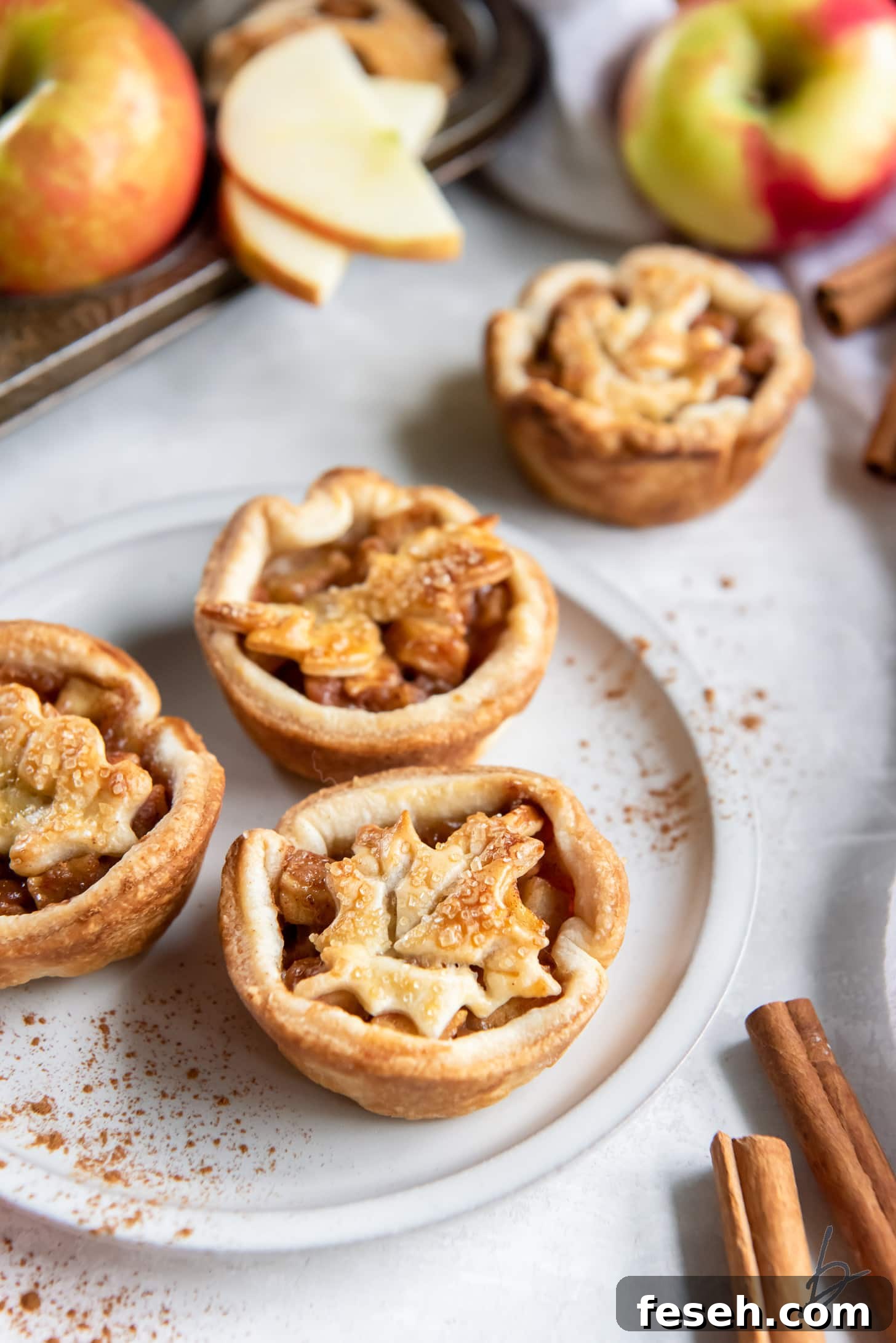 plate with three individual apple pies next to cinnamon sticks.