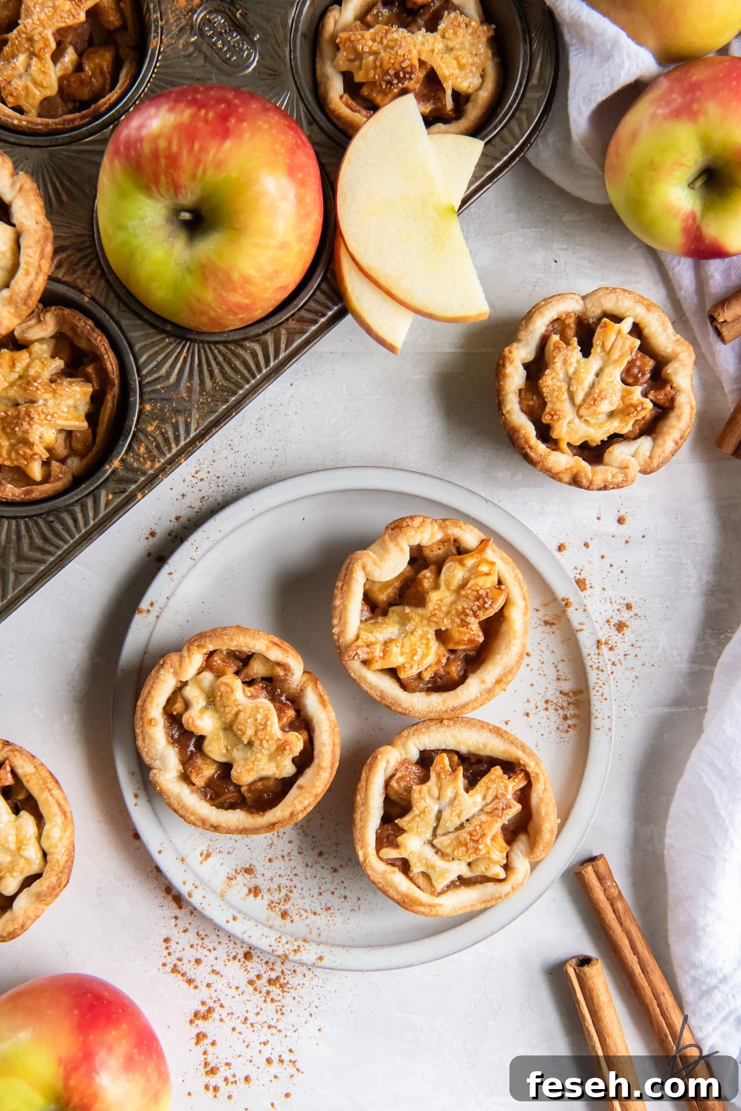 mini apple pies on plate next to apple slices and cinnamon sticks.