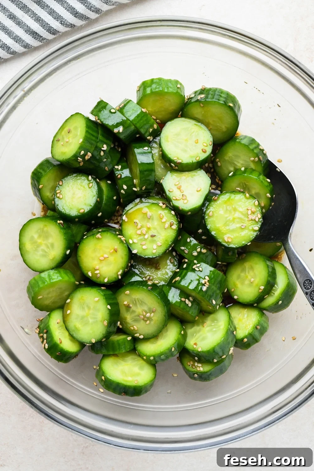 How to make cucumber sesame salad: Dressing poured over sliced cucumbers in a medium sized glass bowl, before marinating.
