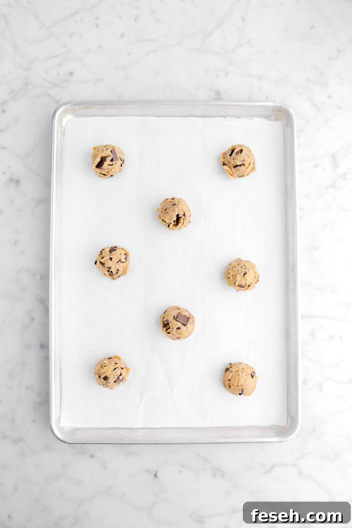 eight cookie dough balls on lined sheet pan.