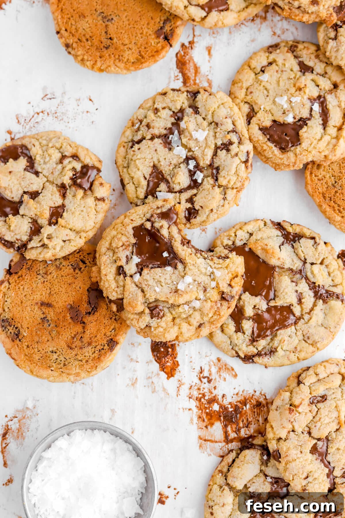 piled chocolate chip cookies on parchment paper with top cookie missing a bite.