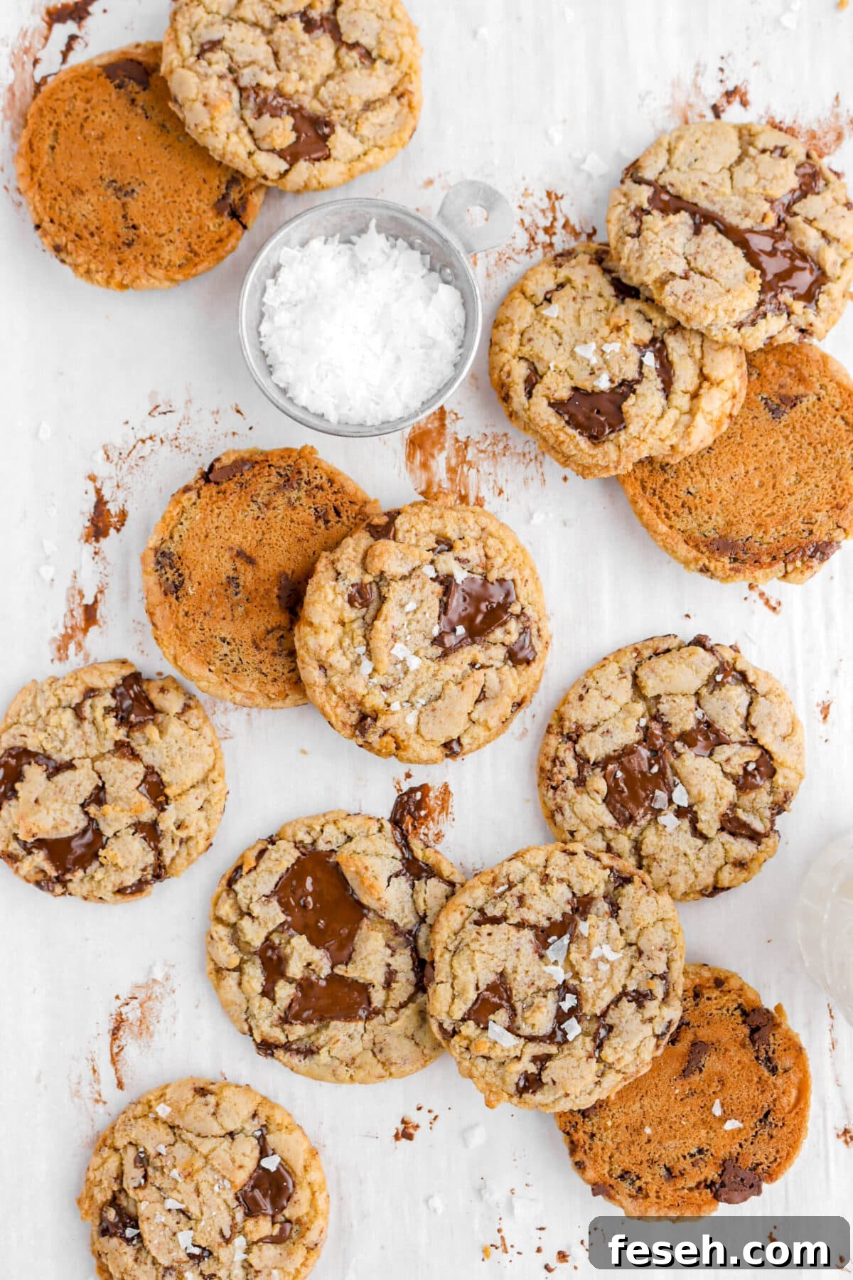 chocolate chip cookies on chocolate stained parchment paper with measuring cup of flaked salt beside.