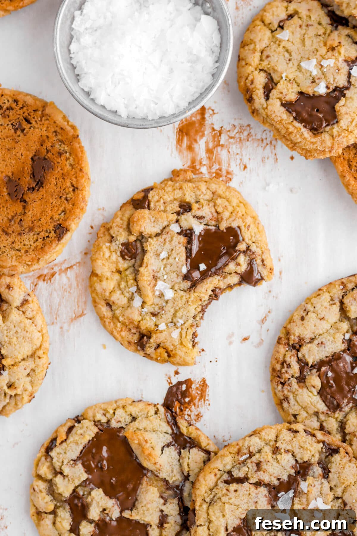 chocolate chip cookie with bite missing on chocolate stained parchment paper with more cookies around.