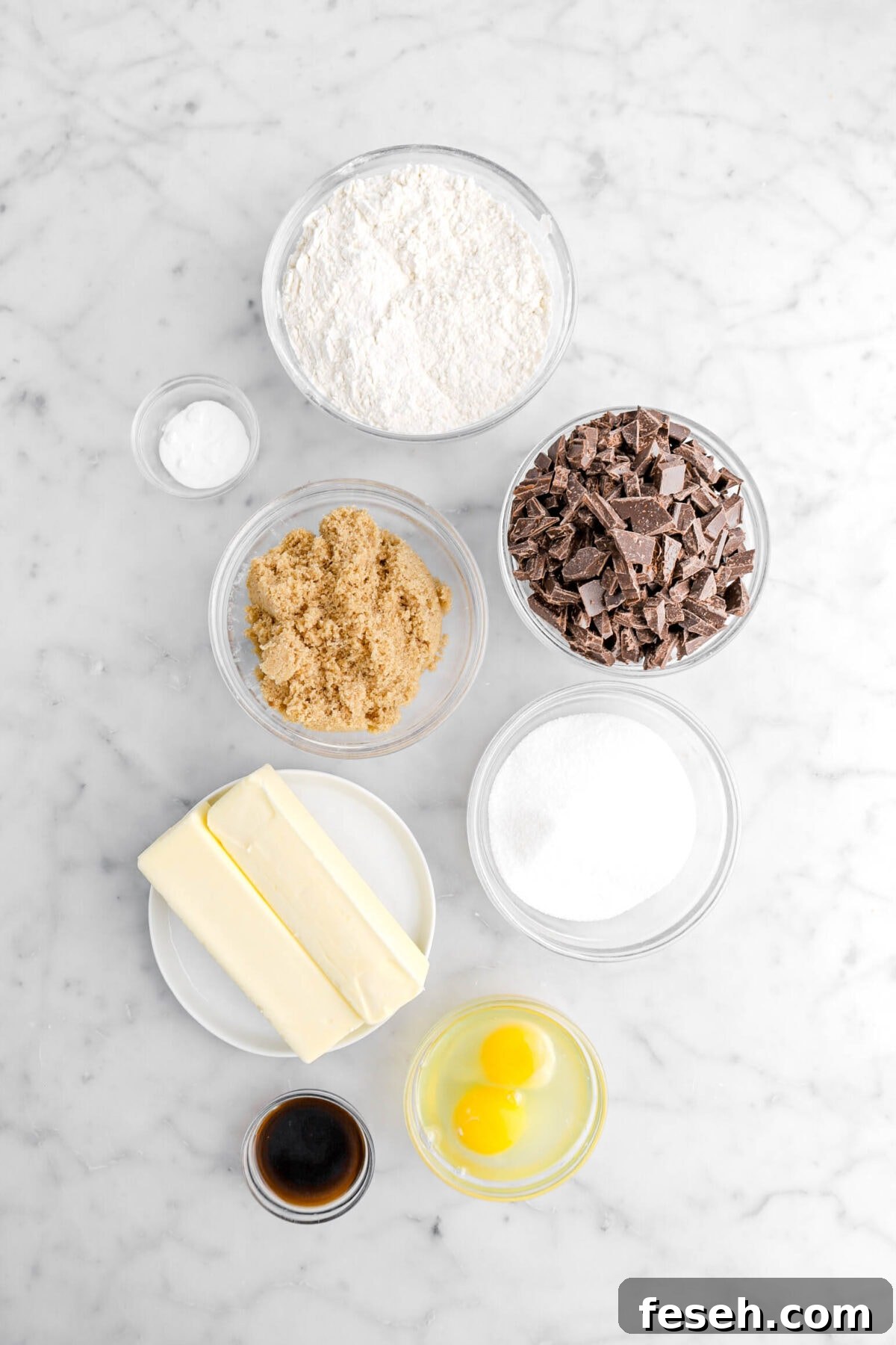 flour, baking soda, brown sugar, chopped chocolate, granulated sugar, two sticks of butter, eggs, and vanilla on marble surface.