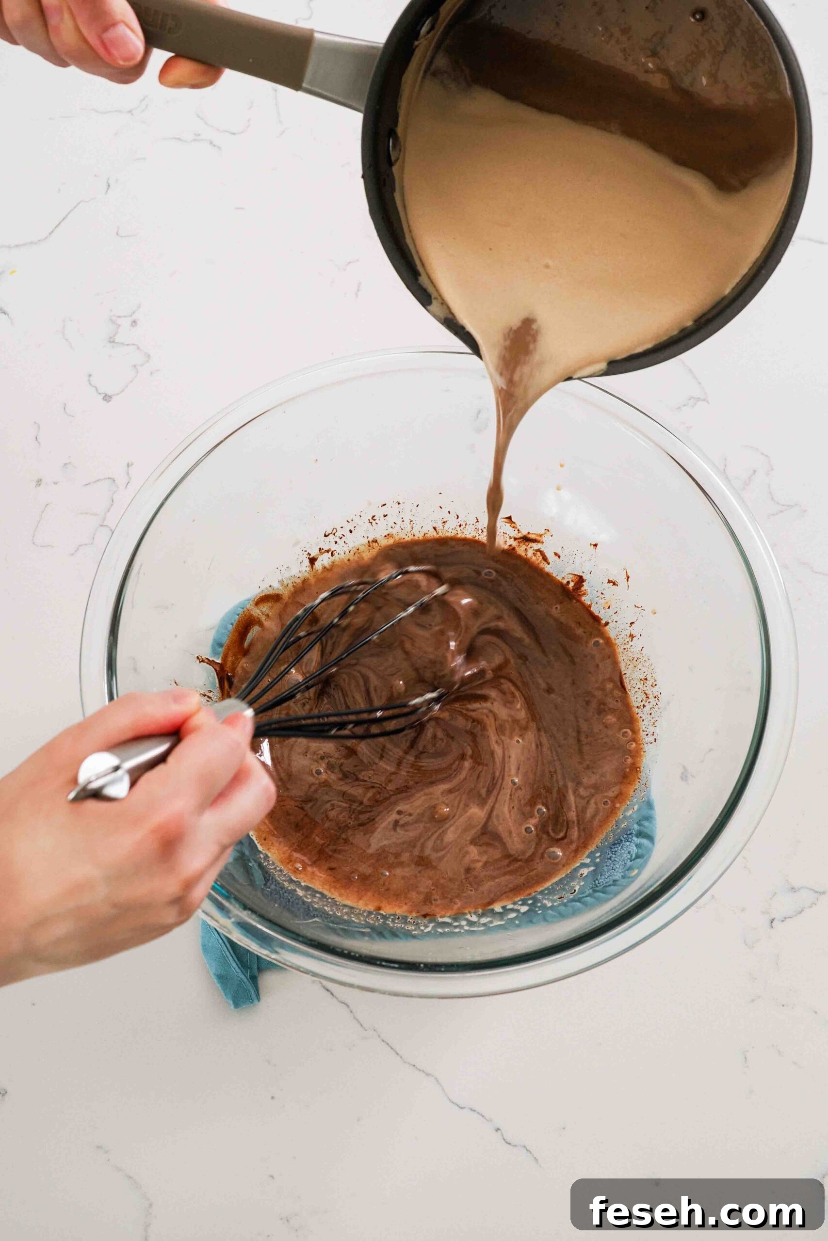 Warmed cream is poured onto chocolate in a large mixing bowl to melt it.