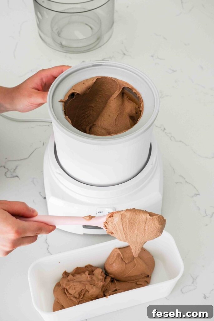 A spatula scoops ice cream out of an ice cream maker and into a freezer container.