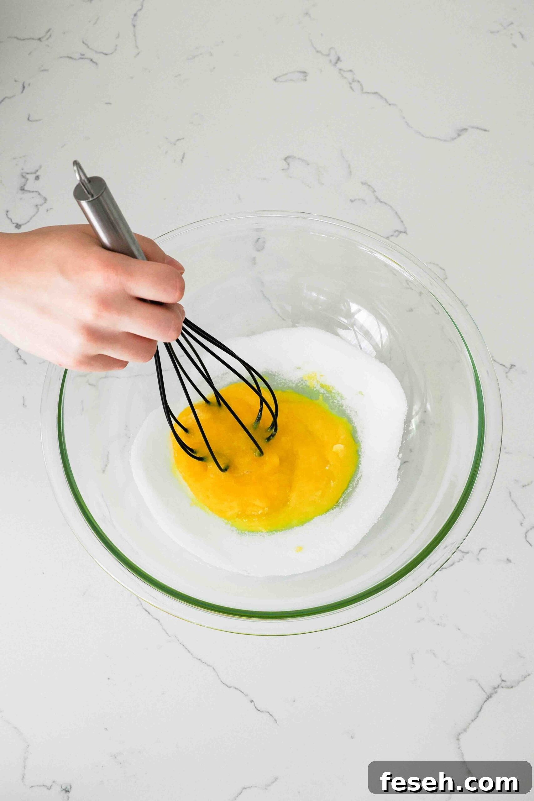 A large balloon whisk stirs together egg yolks and sugar.