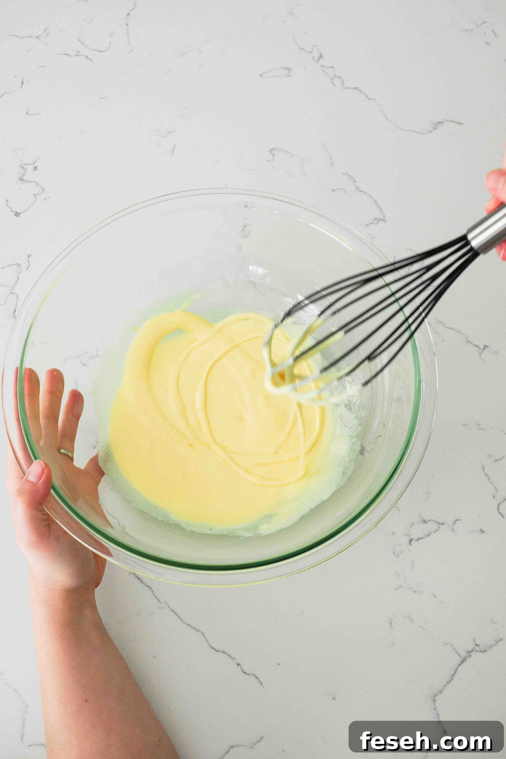 A whisk makes a trail across the top of ribboned egg yolks.