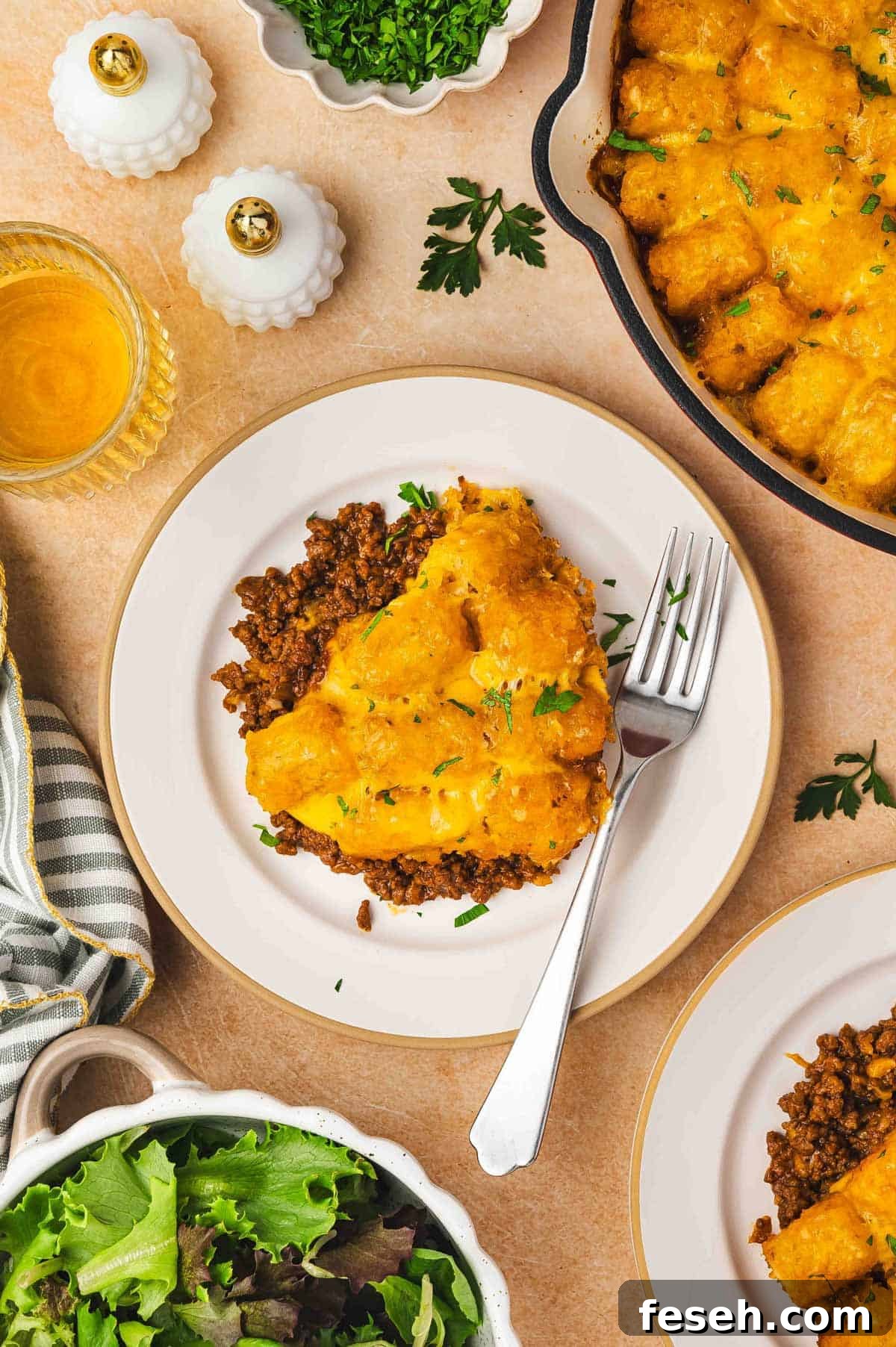 Overhead view of a plate with a serving of sloppy joe tater tot casserole topped with parsley garnish and a fork.