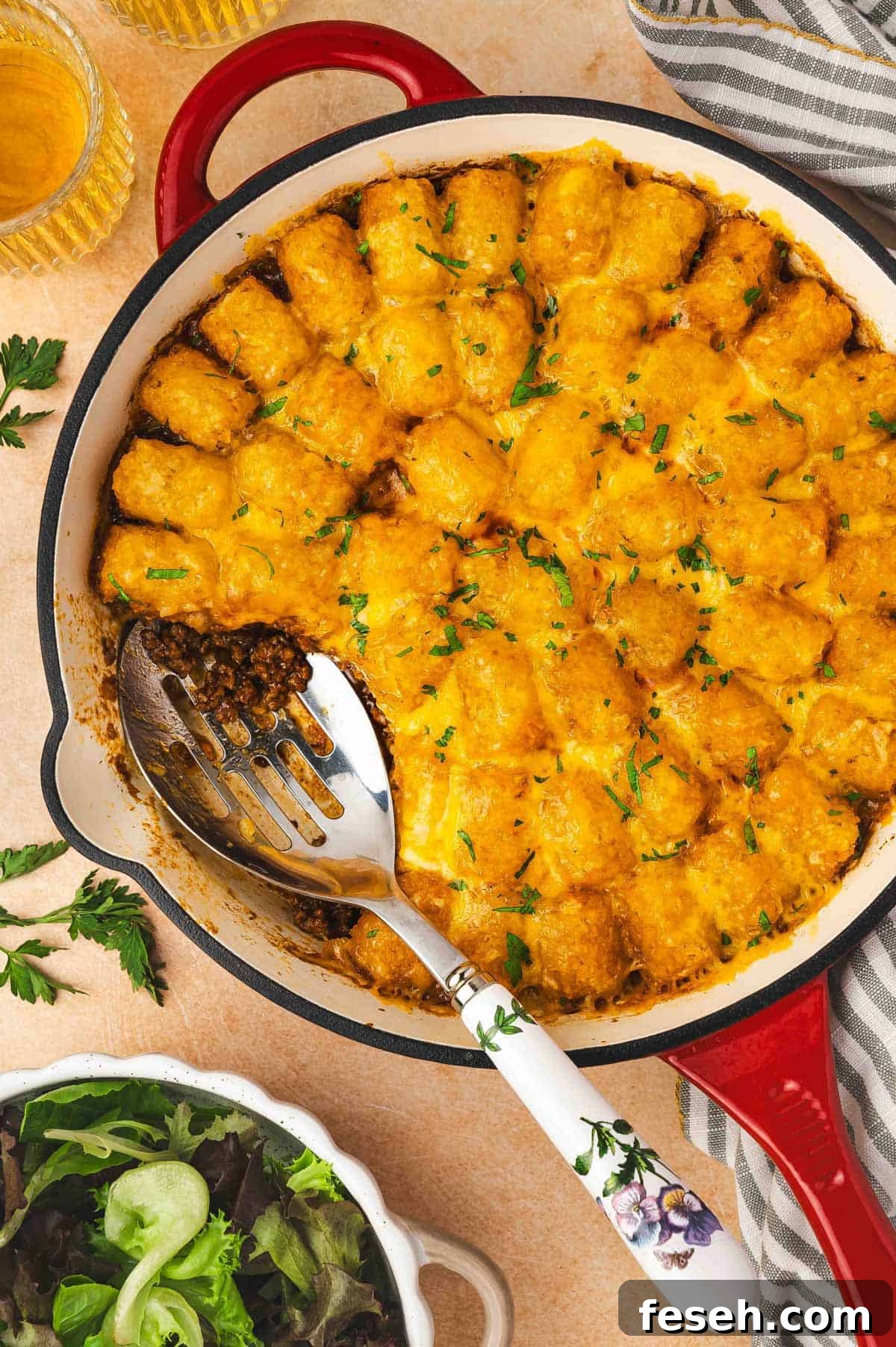 Overhead view of sloppy joe tater tot casserole in a cast iron skillet with a portion scooped out.