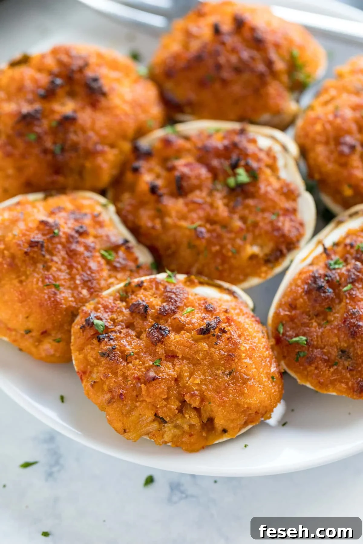 A close up image of a stuffed clam on a white plate with others behind it.