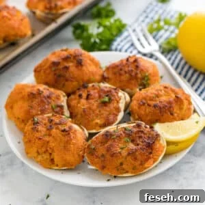 A plate of baked clams with a cocktail fork and lemon wedge on it with the pan, a striped napkin, lemon and parsley behind it.