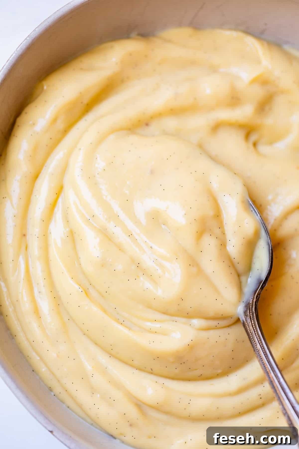 a silver spoon stirring homemade vanilla pastry cream in a bowl.