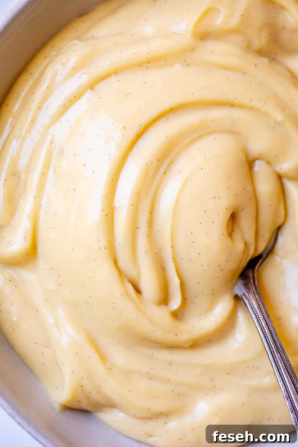 bowl of creamy, vanilla bean flecked Crème Pâtissière being swirled by a spoon.