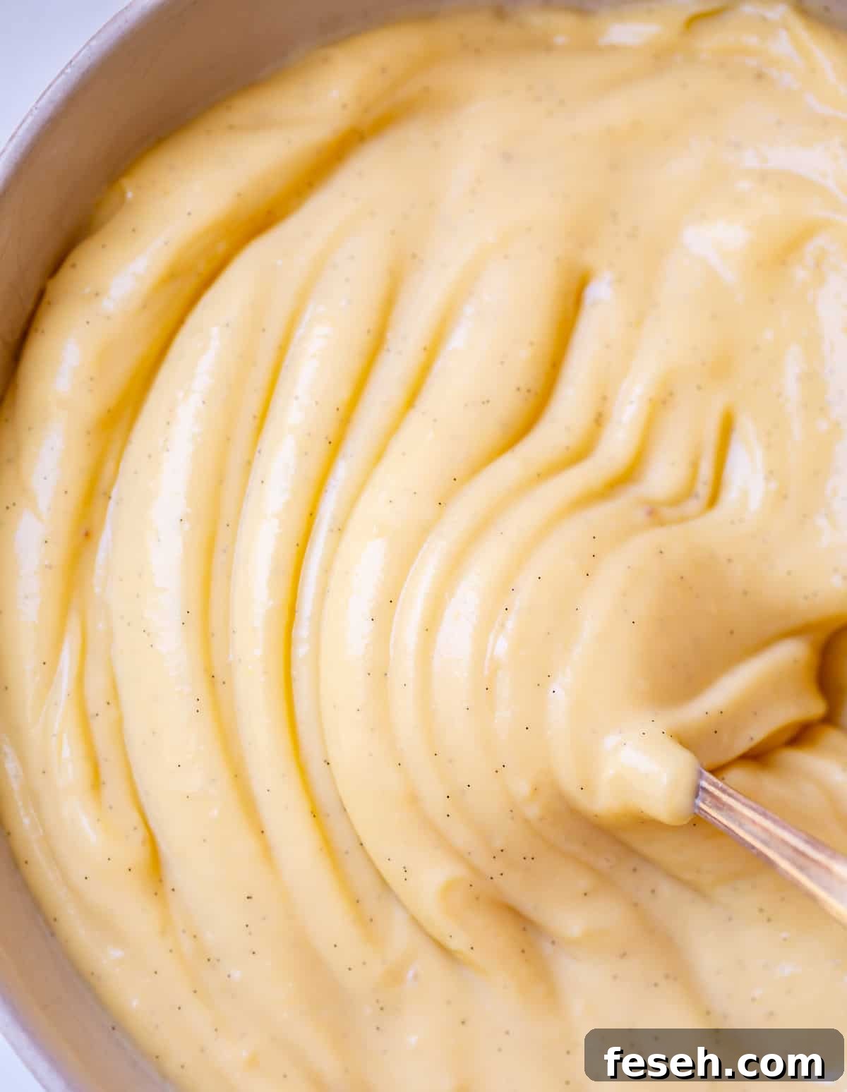 close up of spoon moving through ripples of thick pastry cream in a bowl.