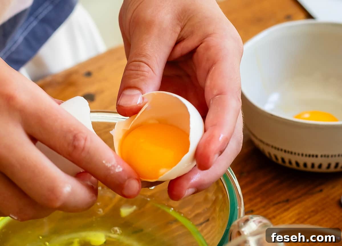 child's hands cracking an egg into a glass mixing bowl.