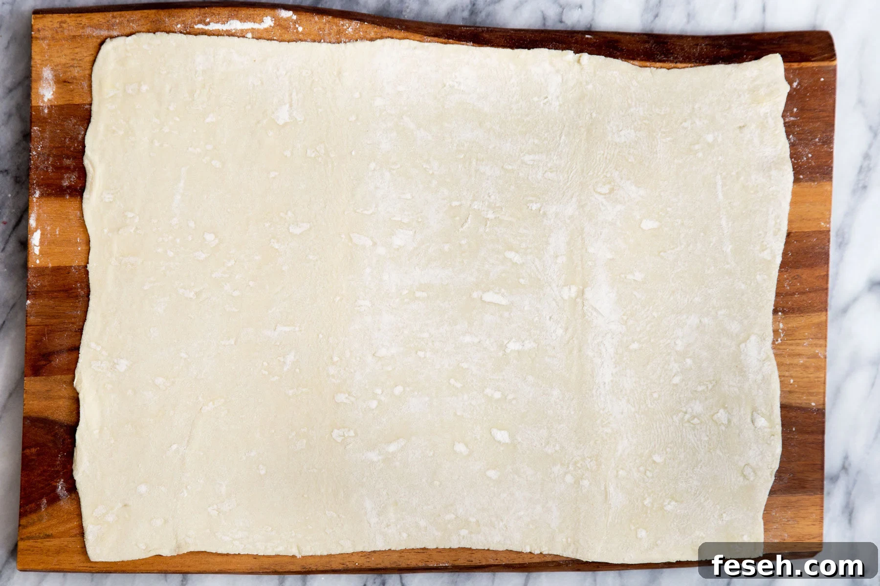 a sheet of puff pastry pasty being rolled out on a chopping board 