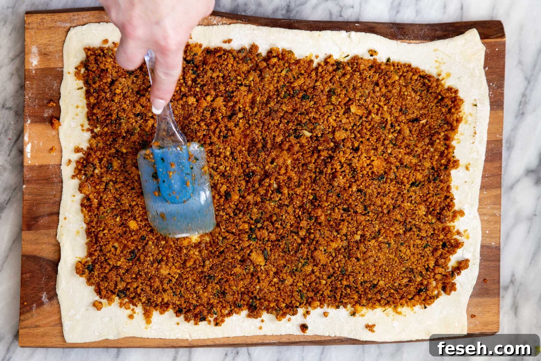 vegan lentil filling being spread out on a sheet of puff pastry 
