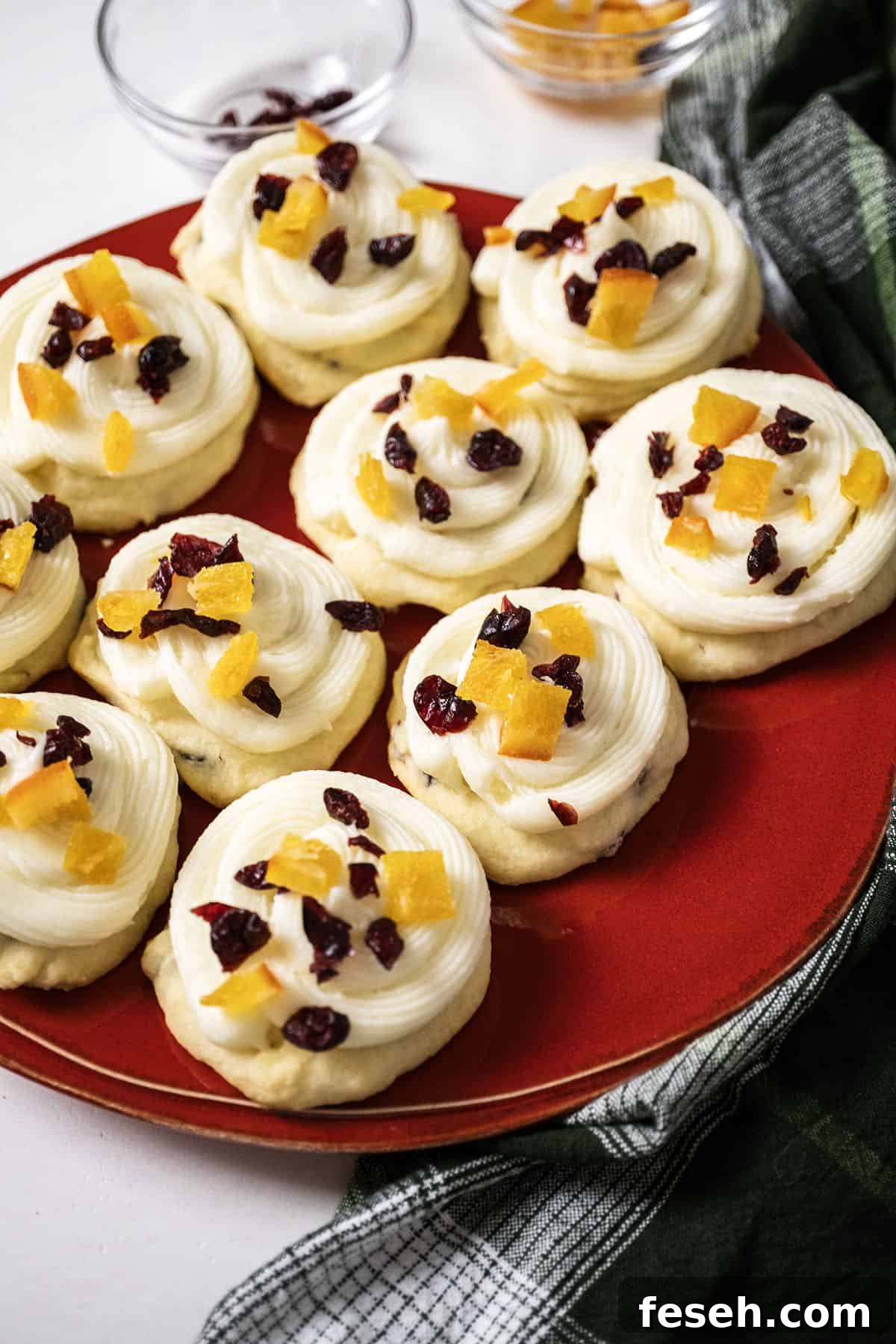 Cranberry and orange shortbread cookies topped with frosting and garnished with dried cranberries and candied oranges.