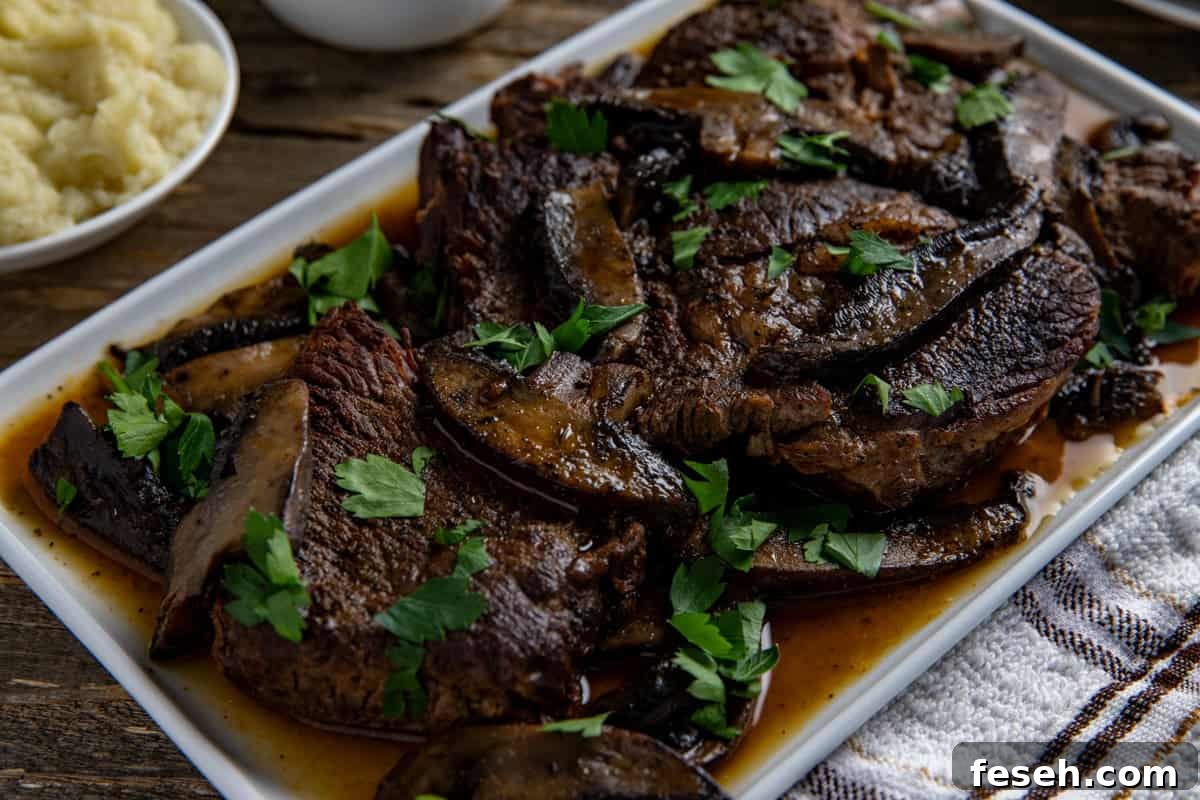Cooked sliced roast topped with mushrooms and sliced portobella mushrooms on a white serving platter.