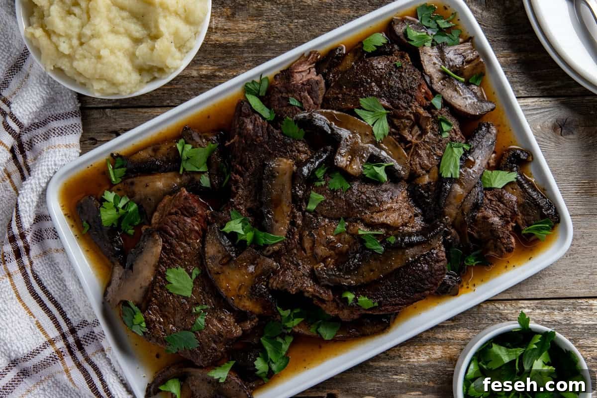 Cooked sliced roast topped with mushrooms and sliced portobella mushrooms on a white serving platter.
