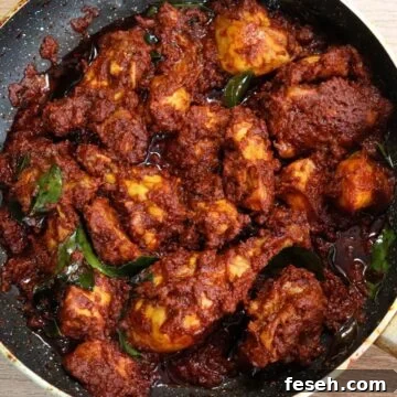 Chicken ghee roast in a black pan. It shows succulent pieces of chicken coated with ghee roasted masala in a black color pan.