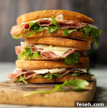 3 salami sandwiches stacked on each other on wooden chopping board