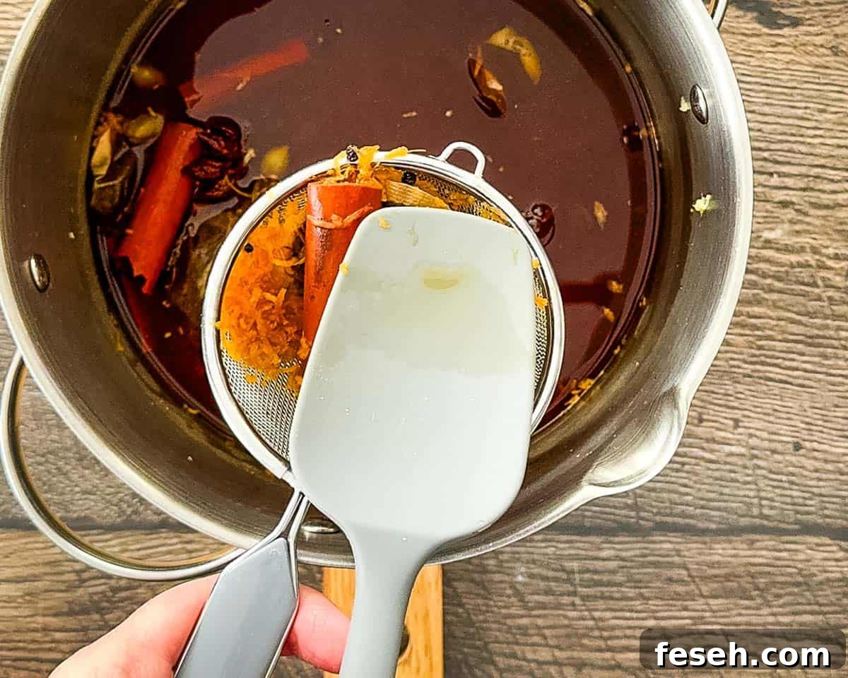 Pressing tea bags and spices through a fine mesh strainer to extract liquid.