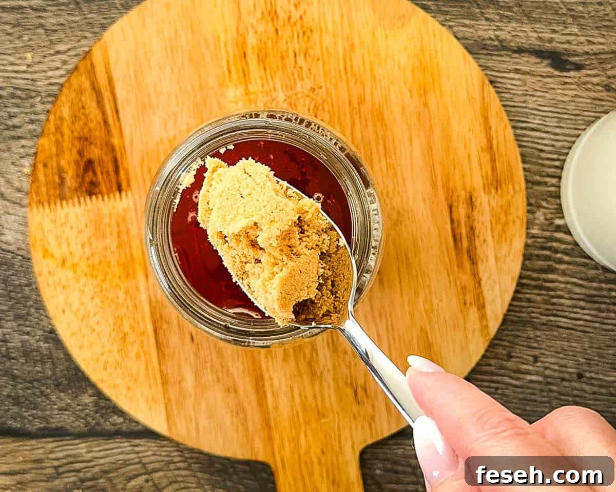 Adding brown sugar to warm chai concentrate in a glass jar before stirring.