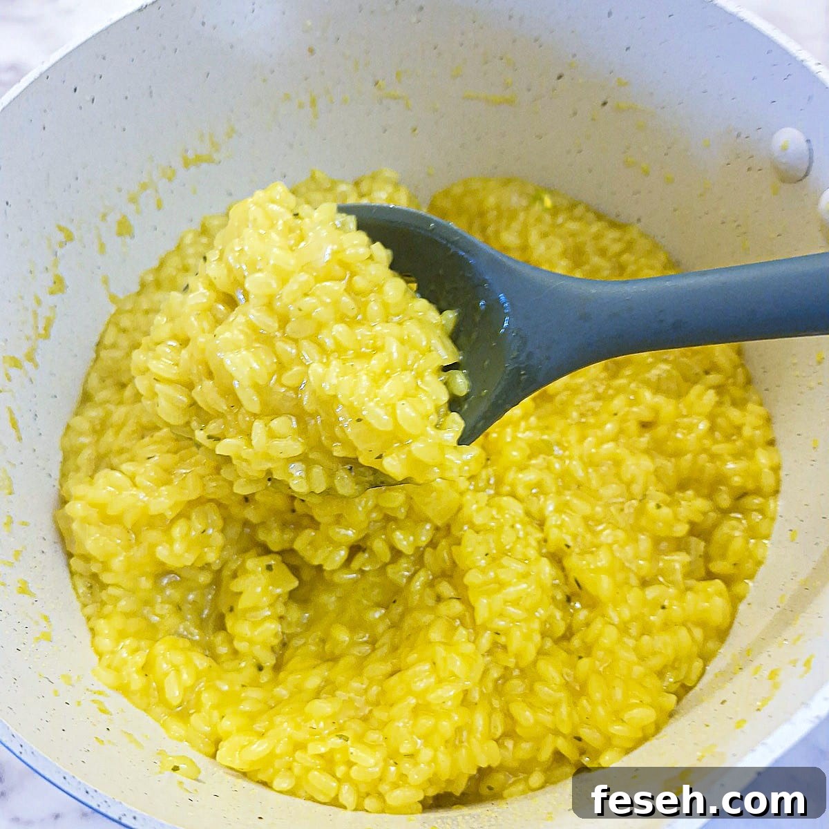Parmesan cheese and butter stirred into the risotto alla Milanese in a saucepan.
