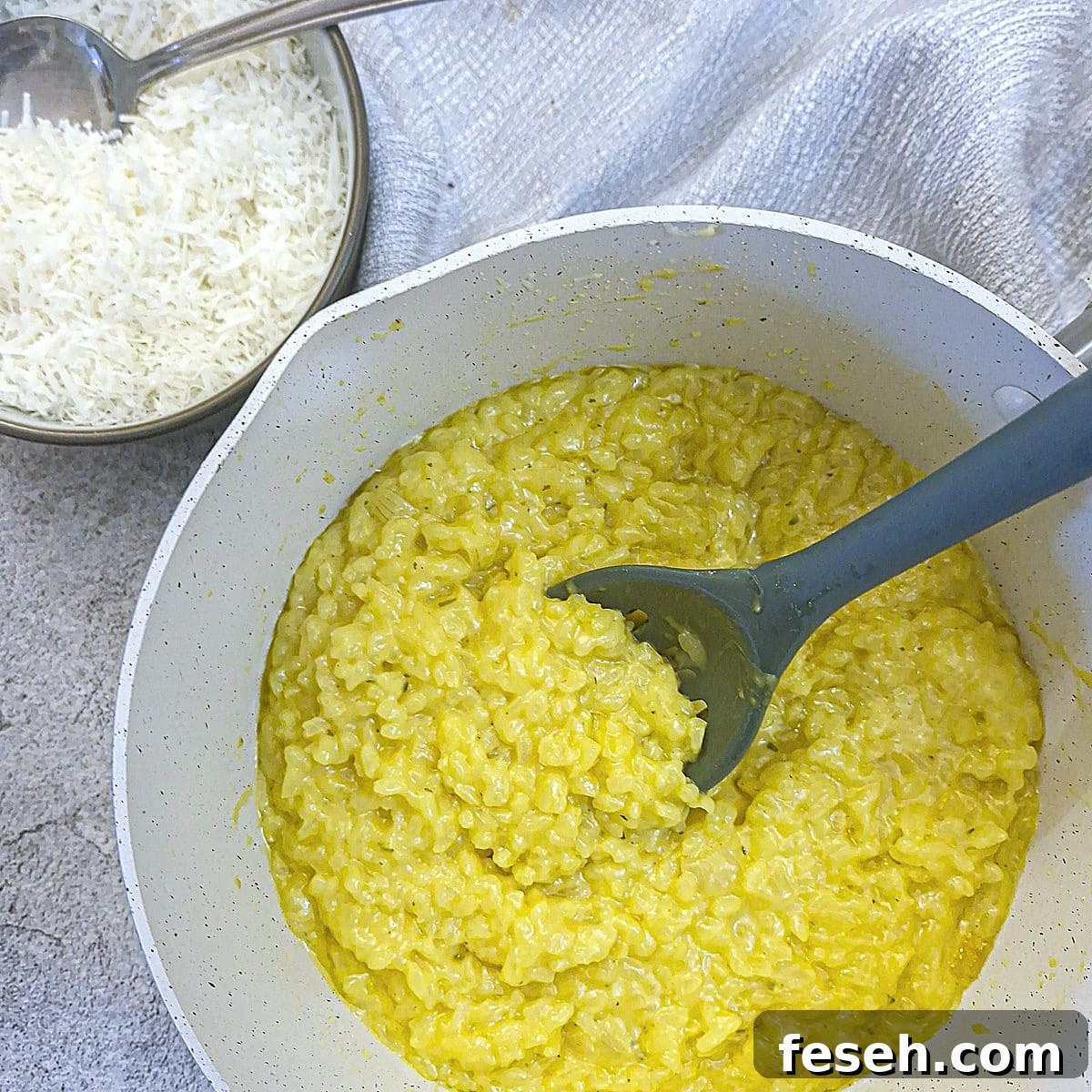 Creamy risotto alla Milanese in a saucepan with a small bowl of parmesan cheese on the side.
