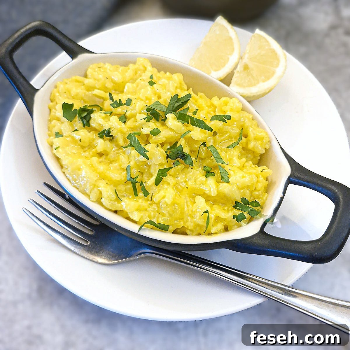 Overhead shot of a dish of risotto alla Milanese garnished with parsley and slices of lemon on the side.