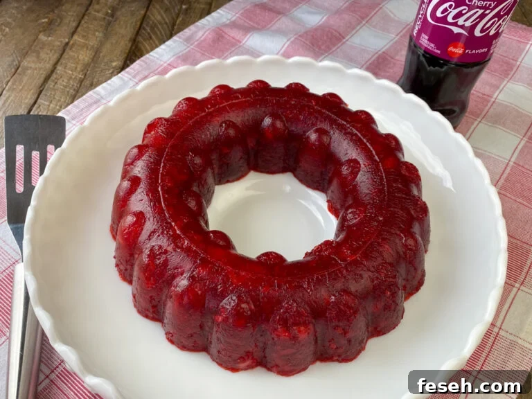 Cherry Coke Jello Salad Recipe — Retro Fizzy Dessert 2 White tray with a cherry coke jello salad dessert made in a jello ring with a server on one side and bottle of cherry coke on the other side on a red and white napkin.