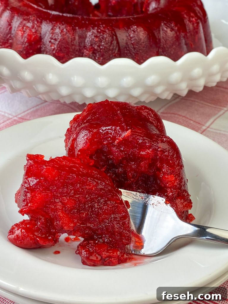 Cherry Coke Jello Salad Recipe — Retro Fizzy Dessert 4 Fork full of coke and cherry jello salad on a stack of white plates with the ring of jello salad in the background.
