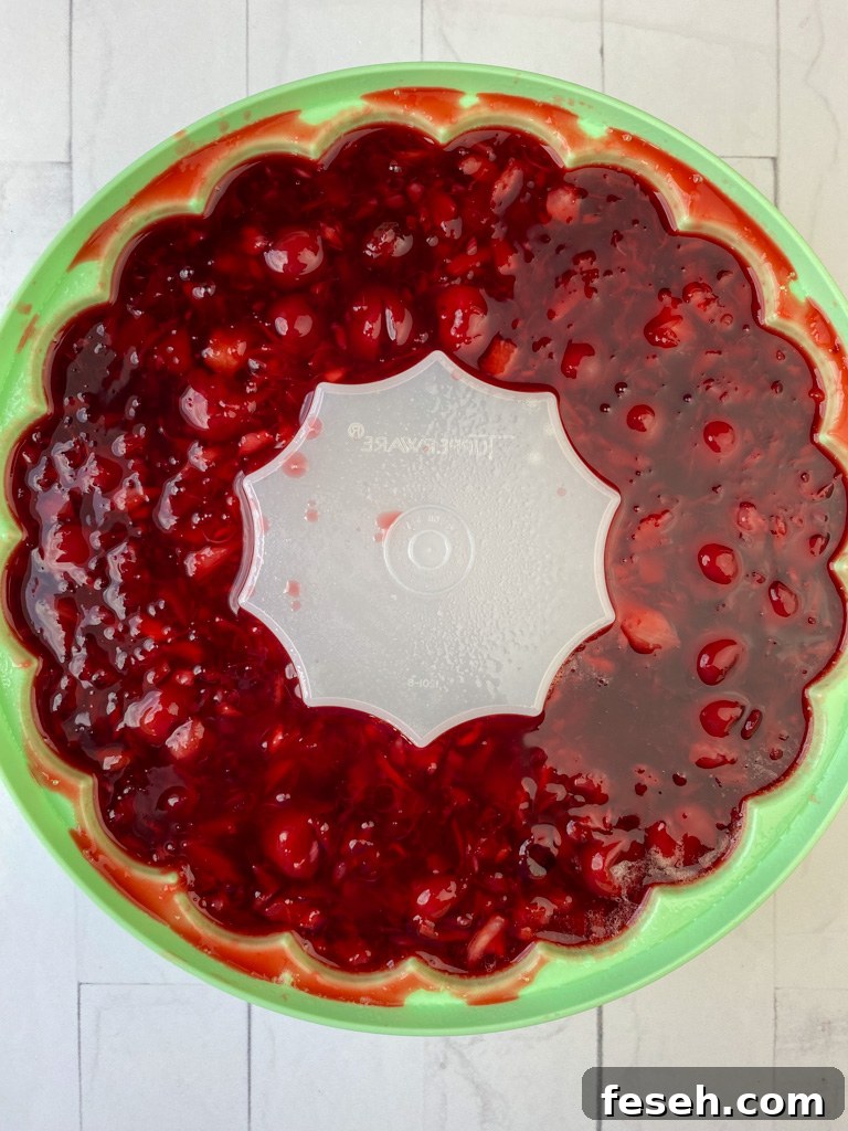 Cherry Coke Jello Salad Recipe — Retro Fizzy Dessert 7 Overhead view of liquid jello mixture poured into a greased green tupperware jello mold on a white counter top.