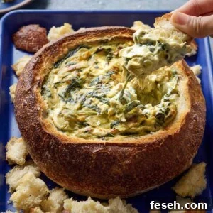 Woman dipping bread into spinach artichoke dip in a bread bowl.